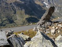 a large rock sitting on top of a rocky hill near a mountain side road in front of a mountainous valley