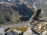 a large rock sitting on top of a rocky hill near a mountain side road in front of a mountainous valley