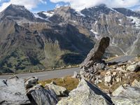 a large rock sitting on top of a rocky hill near a mountain side road in front of a mountainous valley