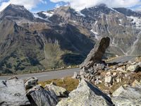 a large rock sitting on top of a rocky hill near a mountain side road in front of a mountainous valley