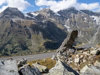 a large rock sitting on top of a rocky hill near a mountain side road in front of a mountainous valley