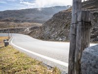 a lone motorcycle riding on the side of the road near mountains and grass in an area with no cars