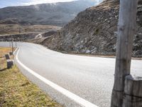 a lone motorcycle riding on the side of the road near mountains and grass in an area with no cars