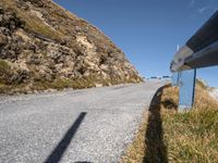 a blue metal railing near a road and mountain scene against a clear blue sky with clouds