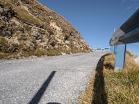 a blue metal railing near a road and mountain scene against a clear blue sky with clouds