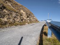 a blue metal railing near a road and mountain scene against a clear blue sky with clouds