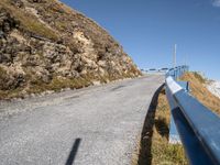 a blue metal railing near a road and mountain scene against a clear blue sky with clouds