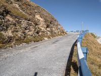 a blue metal railing near a road and mountain scene against a clear blue sky with clouds