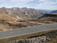 a road winds through mountains with the mountain range in the background in a mountainous landscape