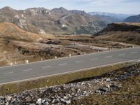 a road winds through mountains with the mountain range in the background in a mountainous landscape