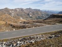 a road winds through mountains with the mountain range in the background in a mountainous landscape