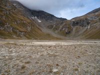 a barren valley is surrounded by mountains under cloudy skies above and below the clouds above