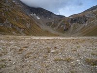 a barren valley is surrounded by mountains under cloudy skies above and below the clouds above