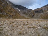 a barren valley is surrounded by mountains under cloudy skies above and below the clouds above