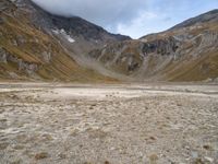 a barren valley is surrounded by mountains under cloudy skies above and below the clouds above