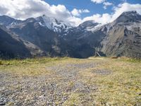 the mountains surrounding the field are rocky and there is grass on the ground beneath it