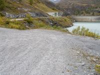 the small gravel path with mountains in the background that has water and green bushes growing next to it