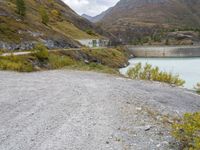 the small gravel path with mountains in the background that has water and green bushes growing next to it