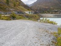 the small gravel path with mountains in the background that has water and green bushes growing next to it