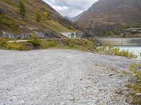 the small gravel path with mountains in the background that has water and green bushes growing next to it