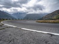 a curve is shown in the middle of a road, with mountains and hills in the distance