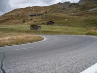 a mountain with an empty road near some houses and a mountain slope behind it that is covered with grass