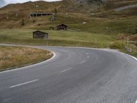 a mountain with an empty road near some houses and a mountain slope behind it that is covered with grass