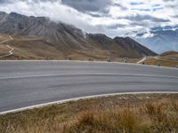 some motorcyclists on the road in the mountains with clouds and the snow capped mountains behind them