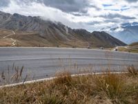 some motorcyclists on the road in the mountains with clouds and the snow capped mountains behind them