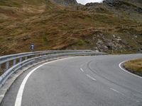 a very winding mountain road by a fenced off road with steep slope in the distance