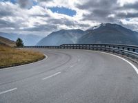 the mountain highway is surrounded by mountains and clouds above it and a curve is in between two lanes that are curving