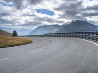 the mountain highway is surrounded by mountains and clouds above it and a curve is in between two lanes that are curving