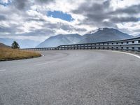 the mountain highway is surrounded by mountains and clouds above it and a curve is in between two lanes that are curving