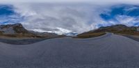 a fish eye view of a long gravel road in mountains surrounding a large cloud,