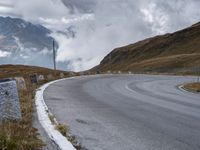 a paved road winding into the middle of the mountain landscape with a lone motorcyclist on it