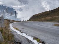 a paved road winding into the middle of the mountain landscape with a lone motorcyclist on it