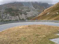 a motorcycle is traveling down a winding road in front of mountains and clouds above it