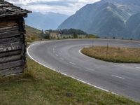 a man riding his bike through an open country road between two mountains, and a log cabin