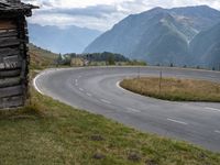 a man riding his bike through an open country road between two mountains, and a log cabin