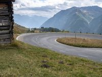 a man riding his bike through an open country road between two mountains, and a log cabin