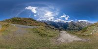 a camera panoramic view of horses grazing on the side of the road and snow capped mountains