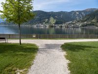 a park bench sits beside a lake overlooking the mountains and a town across the water