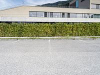 a long hedge lined parking lot with an empty building and a blue sky in the background