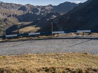 a blue and white train driving along a track in the middle of mountains near a gravel road