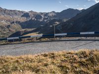 a blue and white train driving along a track in the middle of mountains near a gravel road