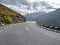 there is a motorcycle riding down a winding road under a cloudy sky in the mountains