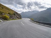 there is a motorcycle riding down a winding road under a cloudy sky in the mountains