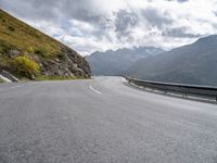 there is a motorcycle riding down a winding road under a cloudy sky in the mountains