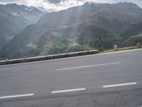 the motorcycle is parked along the side of the mountain road near a mountain range with large mountains behind it