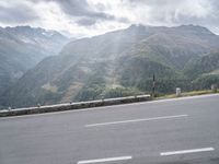 the motorcycle is parked along the side of the mountain road near a mountain range with large mountains behind it
